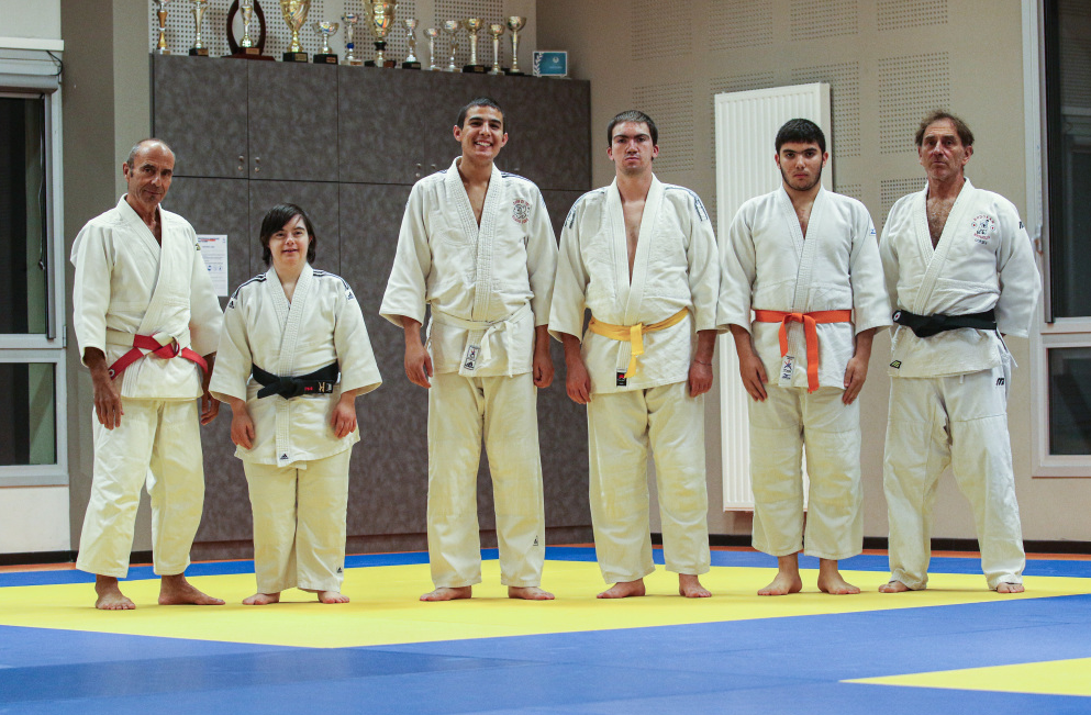 groupe de 5 jeunes en situation de handicap et leur professeur qui posent sur le tatami en tenue de judo.