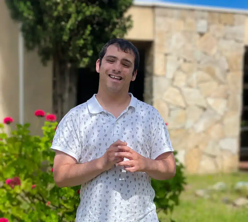 Portrait de Mikaël, un jeune homme approchant de la trentaine. Il porte une chemise à manches courtes et pose avec les jardins de la résidence en arrière plan.